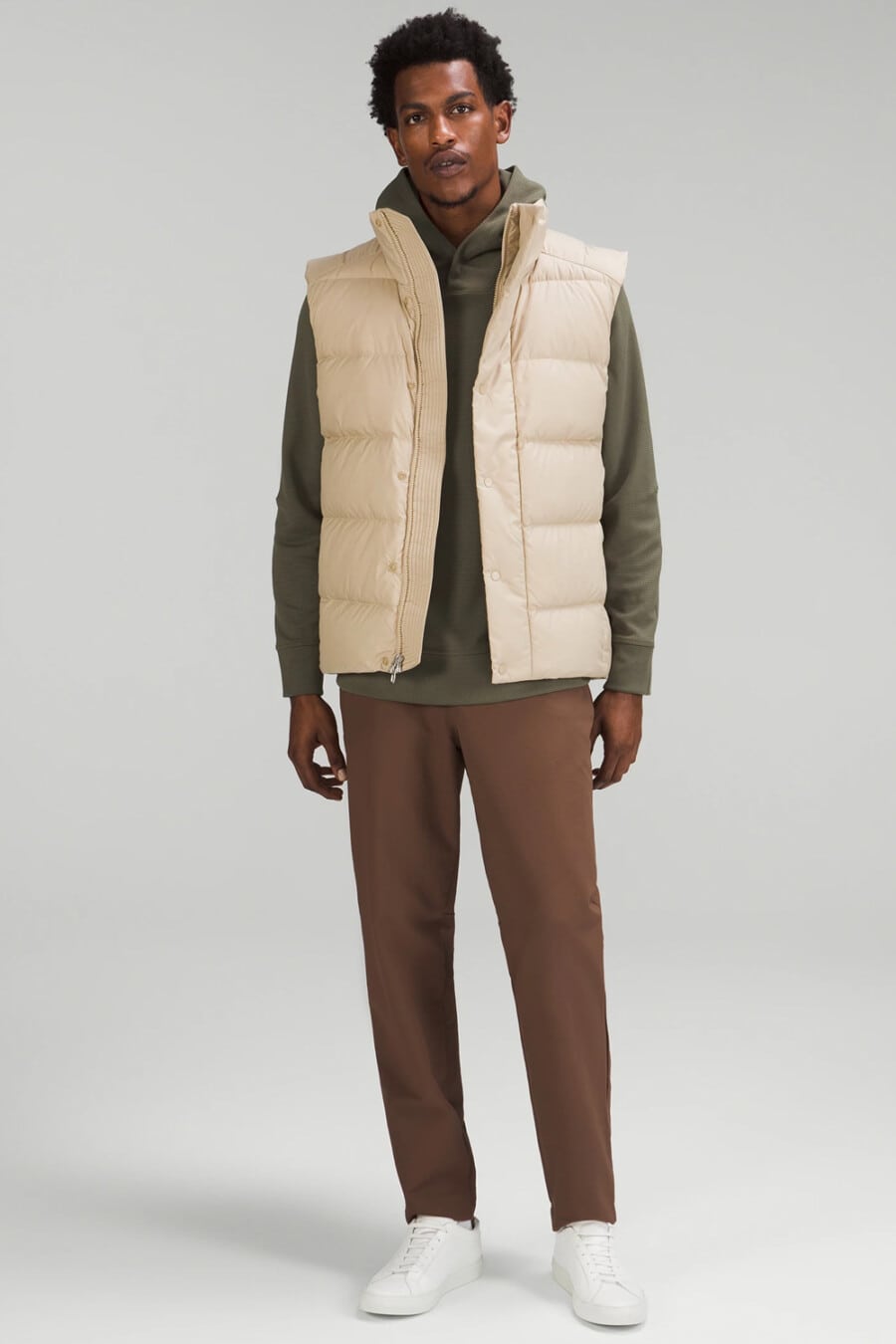 Men's brown pants, green hoodie, cream puffer vest and white sneakers outfit