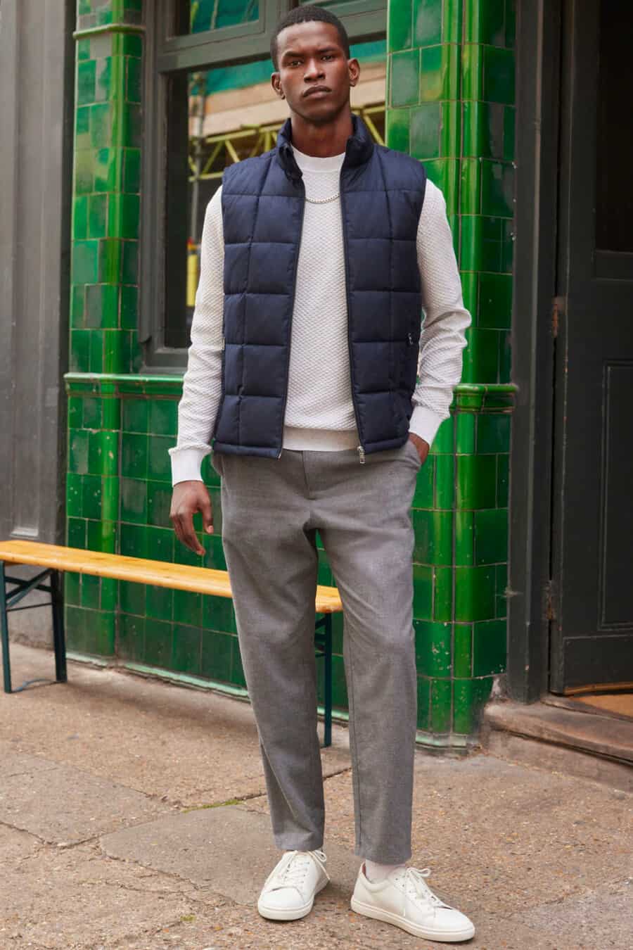 Men's grey pants, white long-sleeve top, navy puffer vest and white sneakers outfit