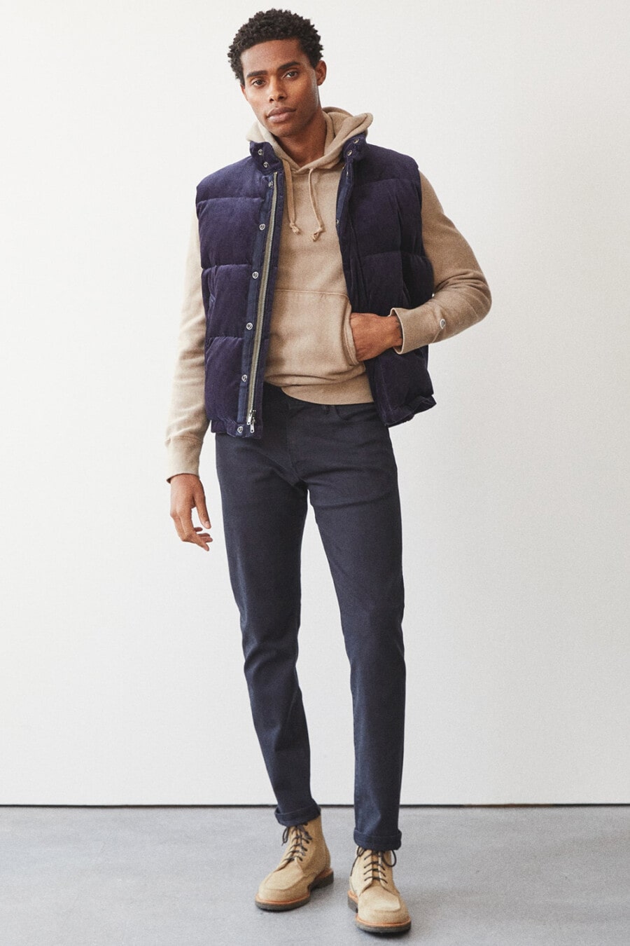 Men's navy pants, light brown hoodie, navy textured puffer vest and beige suede boots outfit