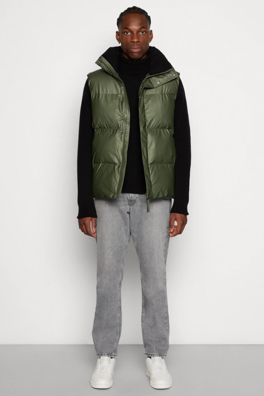 Men's grey jeans, black turtleneck, green puffer vest and white sneakers outfit