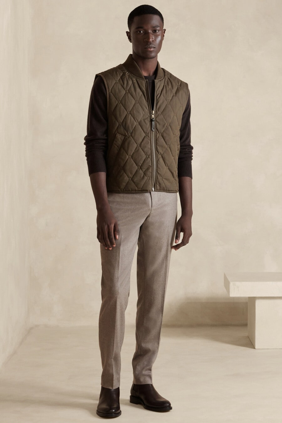 Men's grey chinos, long-sleeve black top, green padded vest and brown leather Chelsea boots outfit