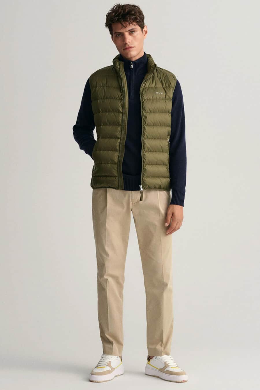 Men's khaki pants, navy quarter zip-neck top, green puffer vest and chunk white/brown sneakers outfit
