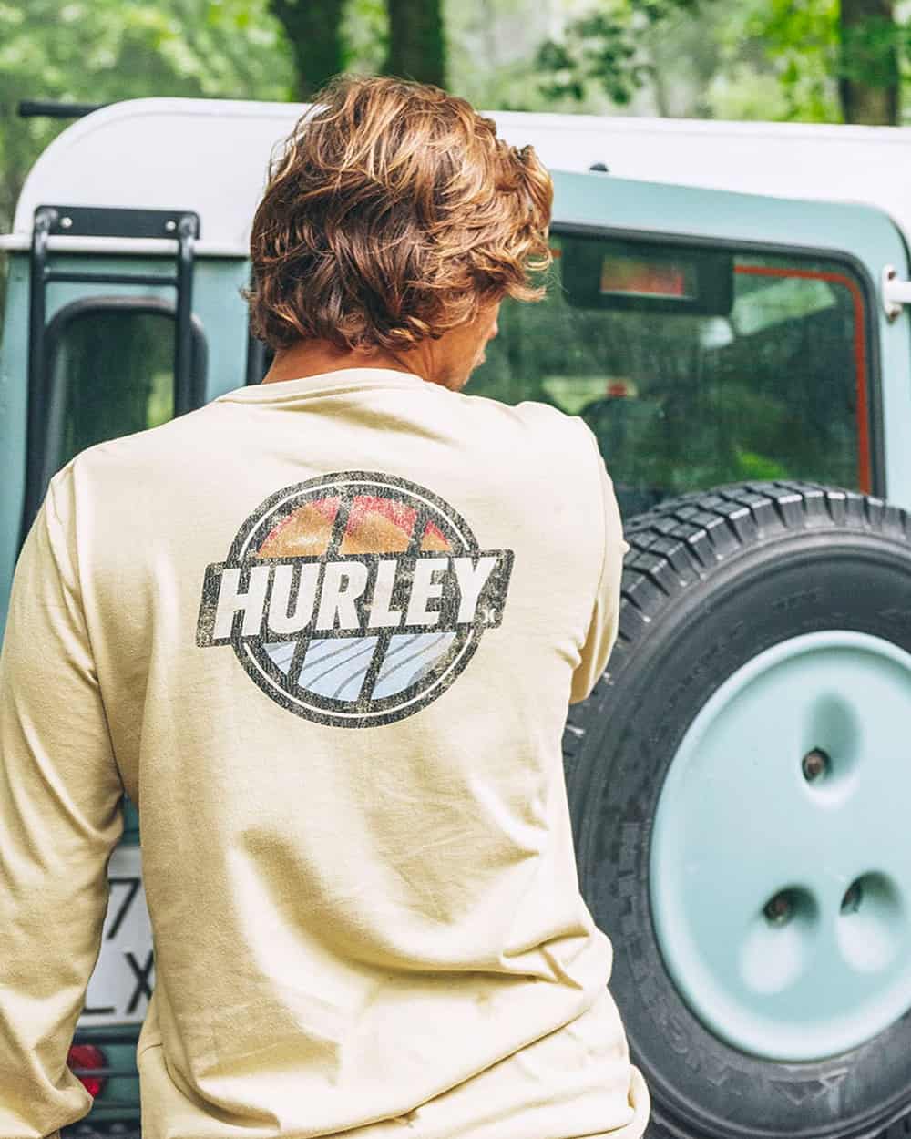 Man in front of jeep wearing a washed yellow Hurley printed back logo top