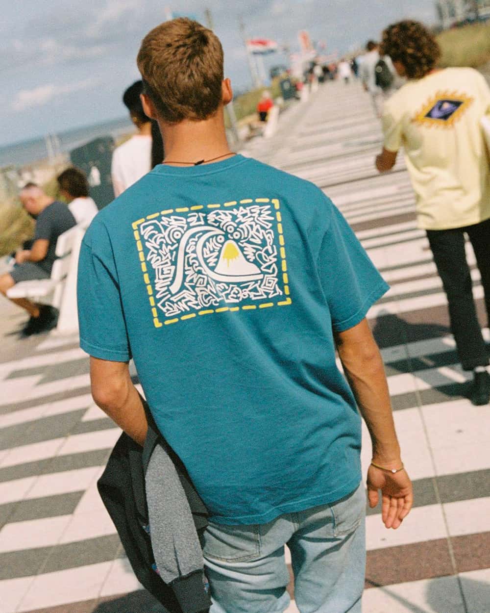 Man wearing a teal back printed Quicksilver T-shirt with light wash blue jeans