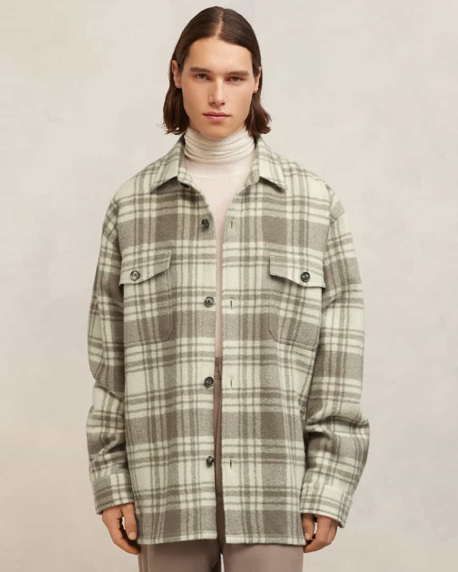 Man wearing oversized Ami Paris flannel shirt in green/brown check over an off-white turtleneck with brown pants