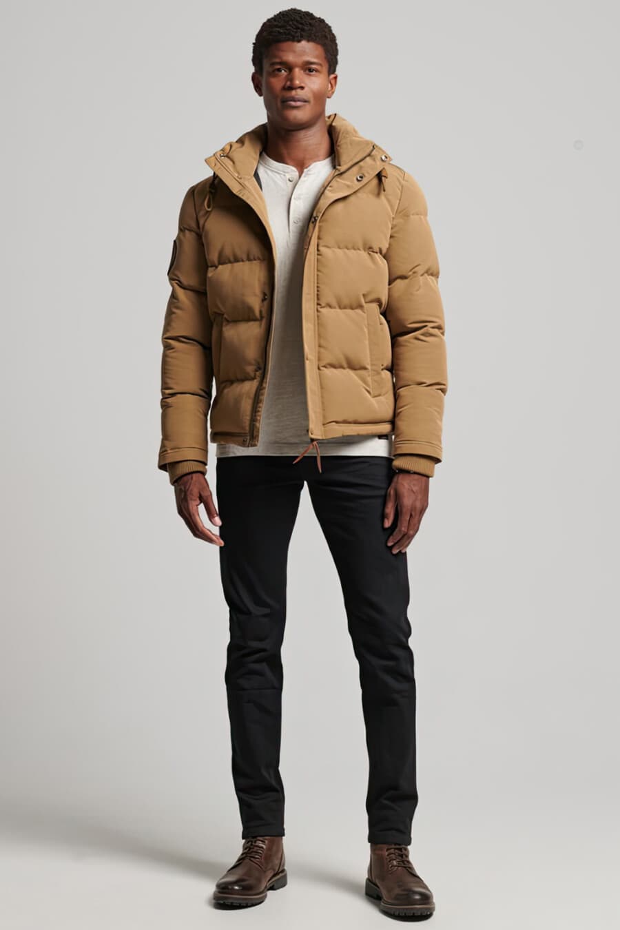 Men's black jeans, white Henley top, cropped camel puffer jacket and brown leather boots outfit