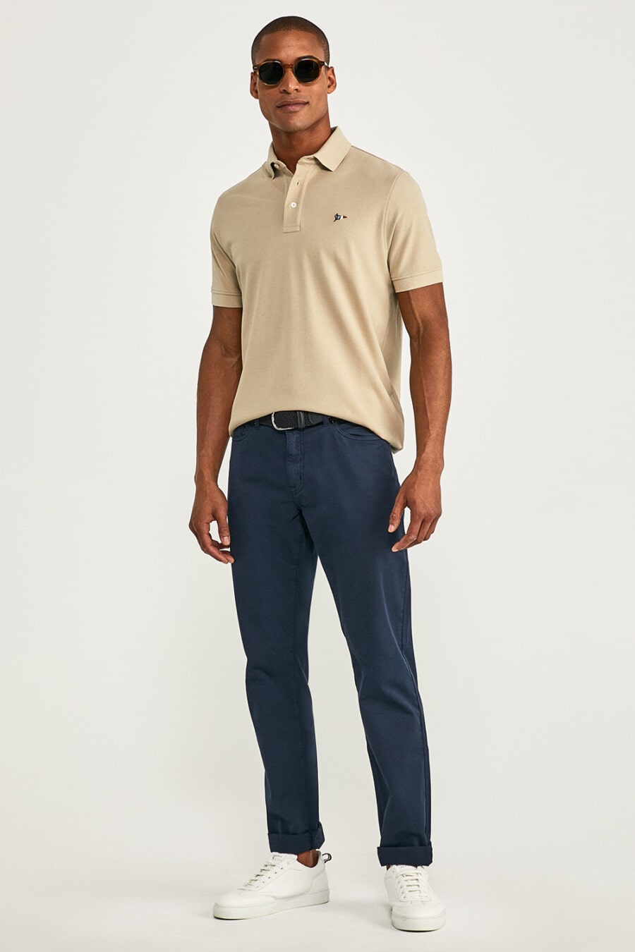 Men's navy chinos, light brown polo shirt, round lens sunglasses and white sneakers worn sockless outfit