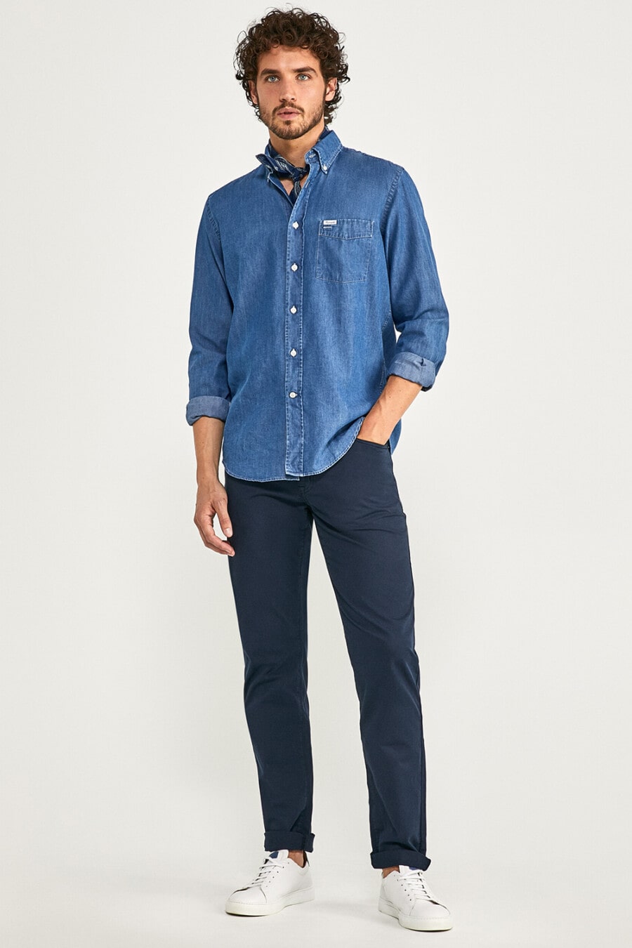 Men's navy chinos, blue denim shirt, blue neckerchief and white sneakers worn sockless outfit