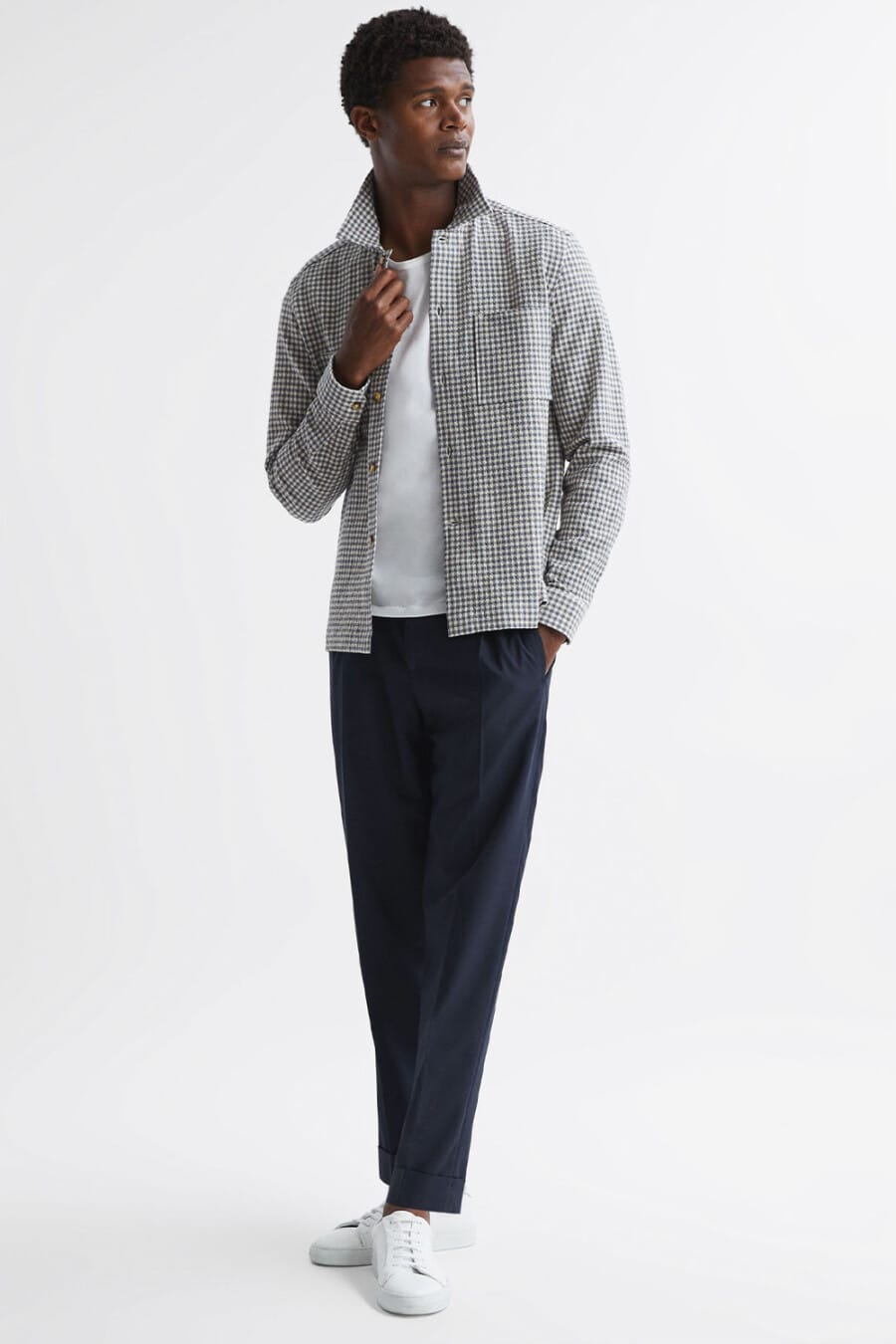 Men's navy pants, white T-shirt, grey houndstooth shacket and white sneakers worn sockless outfit