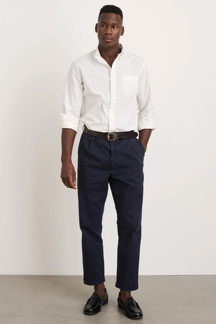 Men's cropped navy chinos, tucked in white shirt, brown leather belt and black leather penny loafers outfit