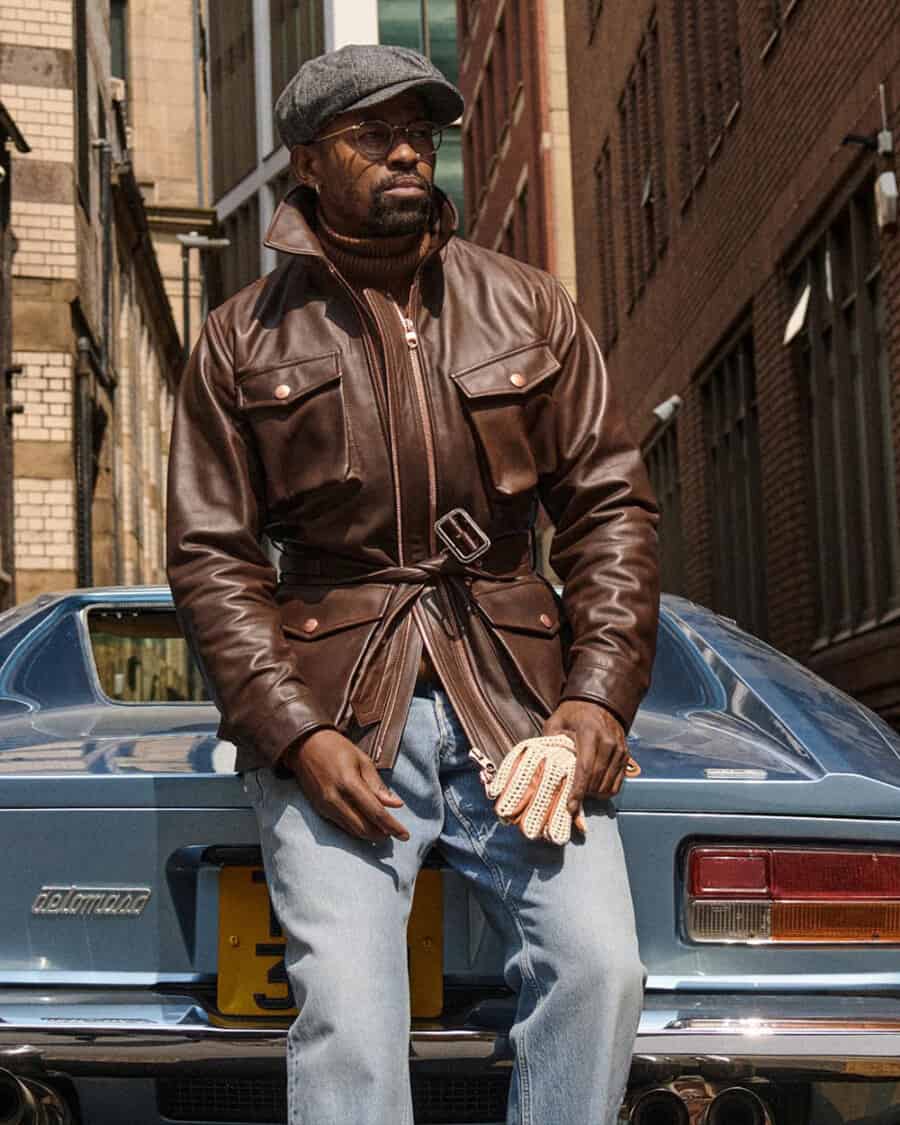 Black man wearing Private White V.C. The Leather Twin Track jacket with light wash jeans and grey baker boy hat