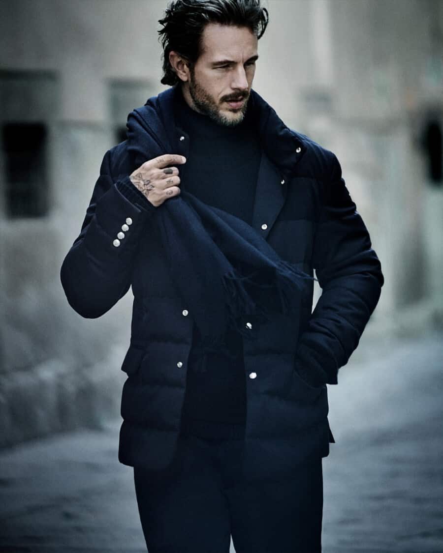 Man wearing a smart navy Moncler long puffer jacket with navy pants, a navy turtleneck and navy scarf