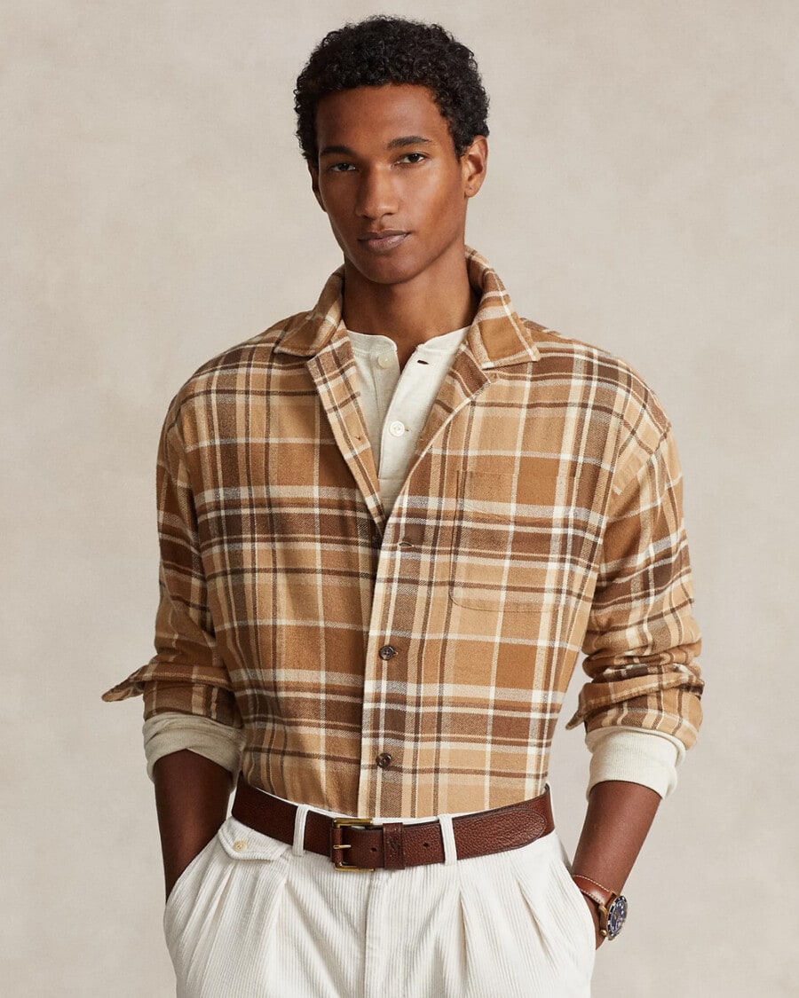 Man wearing brown/camel checked flannel shirt over a Henley top tucked into white pleated corduroy pants