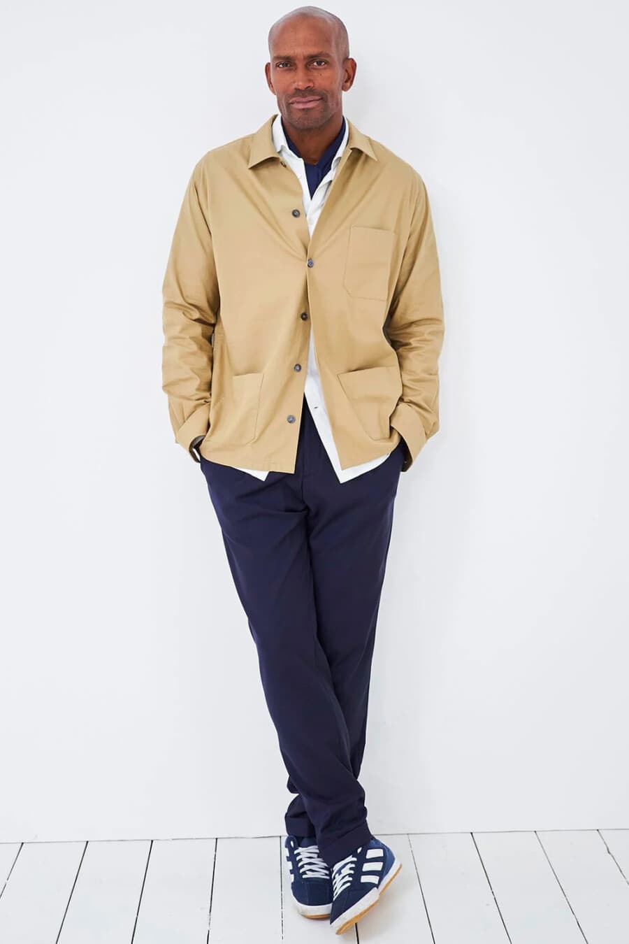 Men's navy chino pants, white shirt, beige cotton shacket and blue adidas Gazelle sneakers outfit