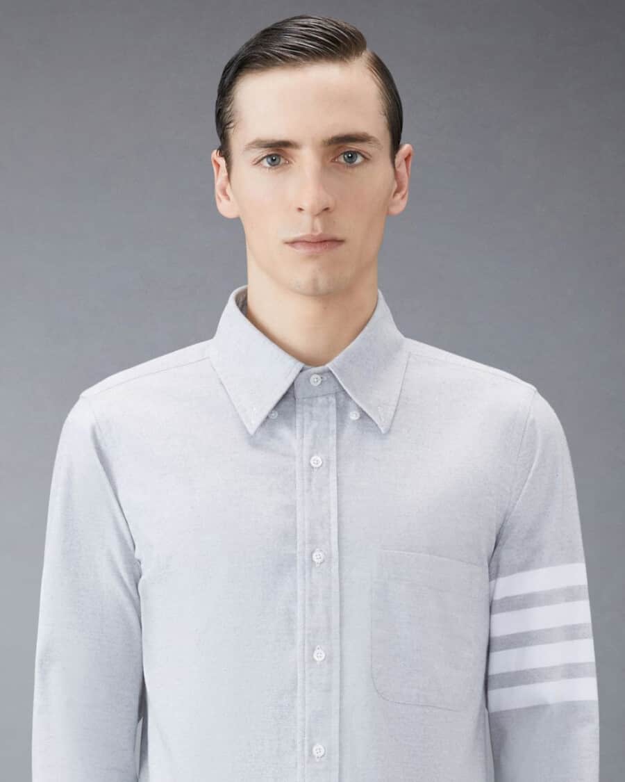 Close up of aman wearing light grey Thom Browne flannel shirt with 4 white stripes branding to the left arm