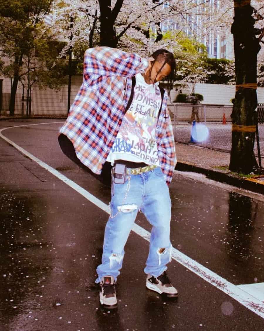 Travis Scott wearing oversized Balenciaga flannel shirt with printed T-shirt, ripped blue jeans and chunky sneakers