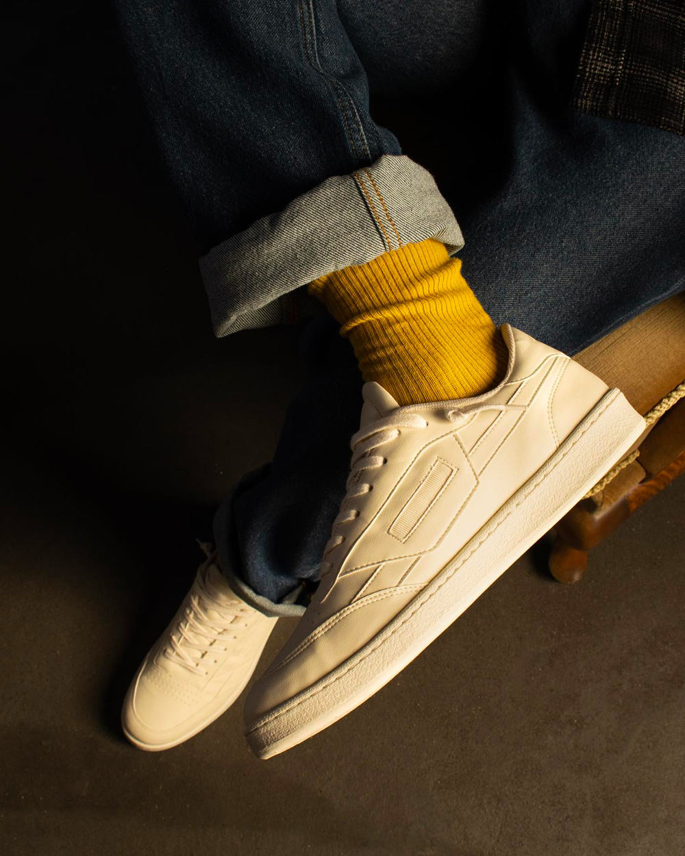 White Oliver Cabell sneakers worn on feet with turned up denim jeans and yellow socks