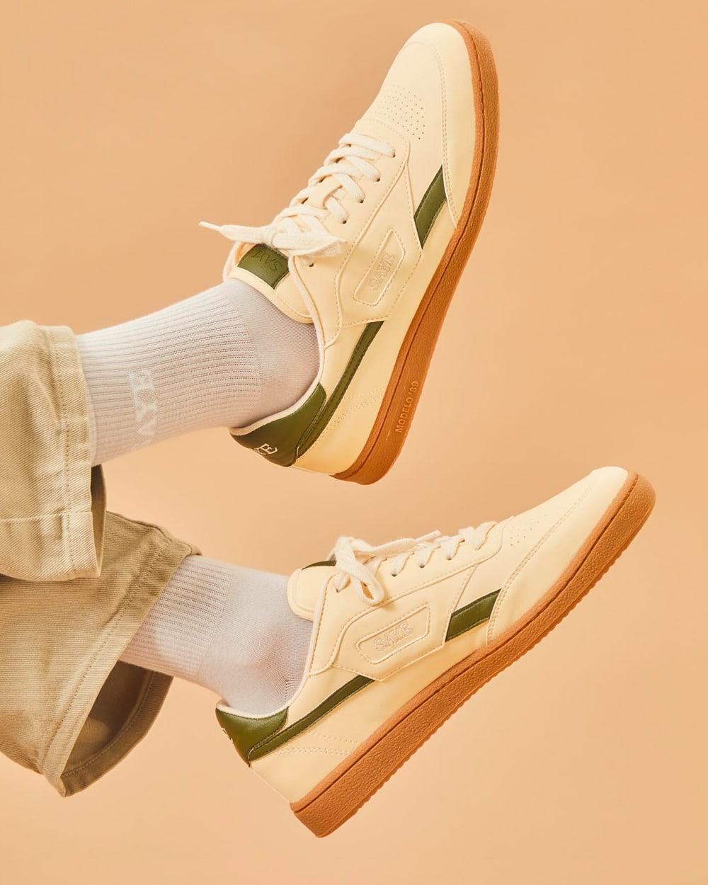 Men's SAYE off-white and green gumsole sneakers worn on feet with white socks and khaki pants