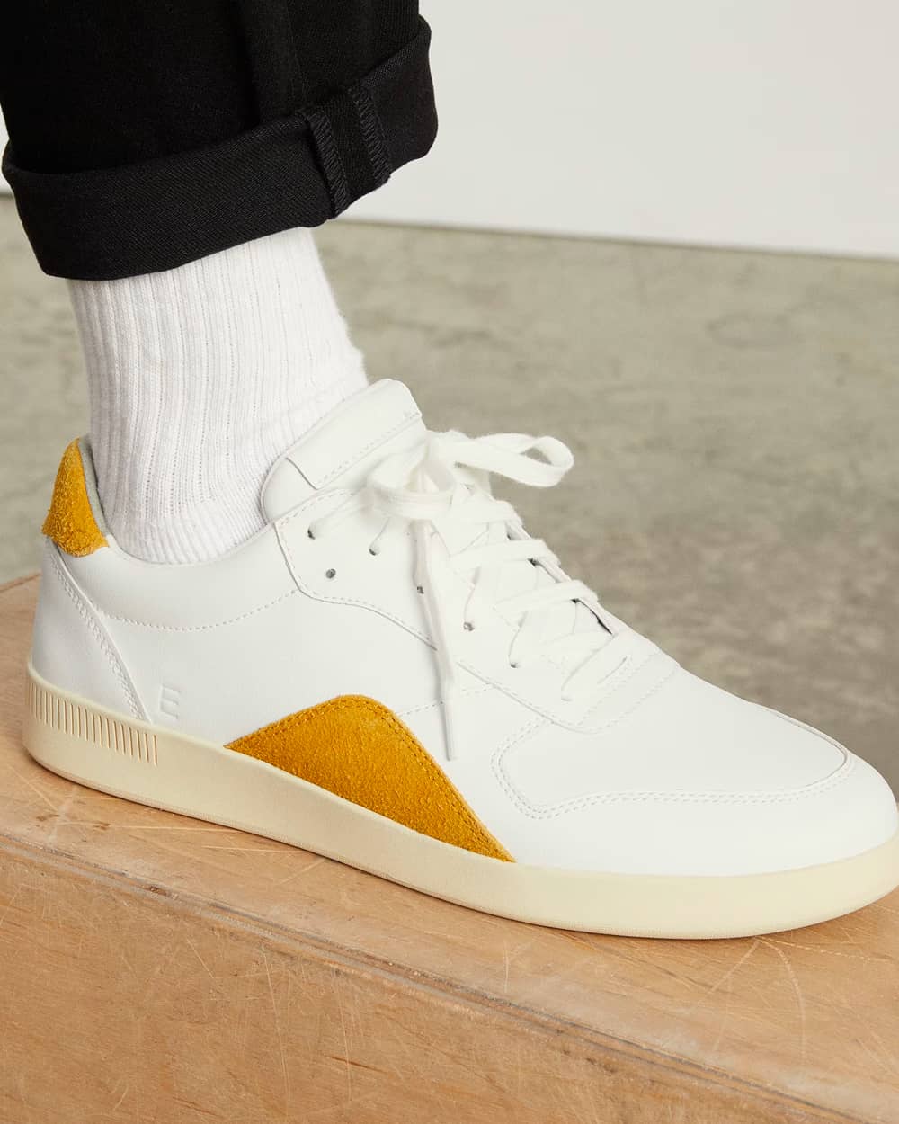 Everlane The ReLeather Court Sneakers in white and yellow worn on feet with white socks and black pants