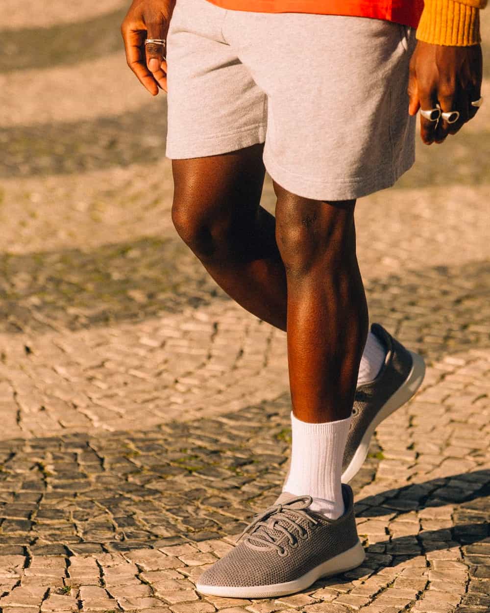 Man wearing AllBirds Tree Runner sneakers on feet with white socks and grey jersey shorts