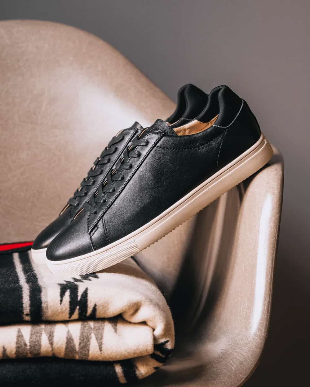 A pair of black grain leather CLAE sneakers with white sole on leather chair