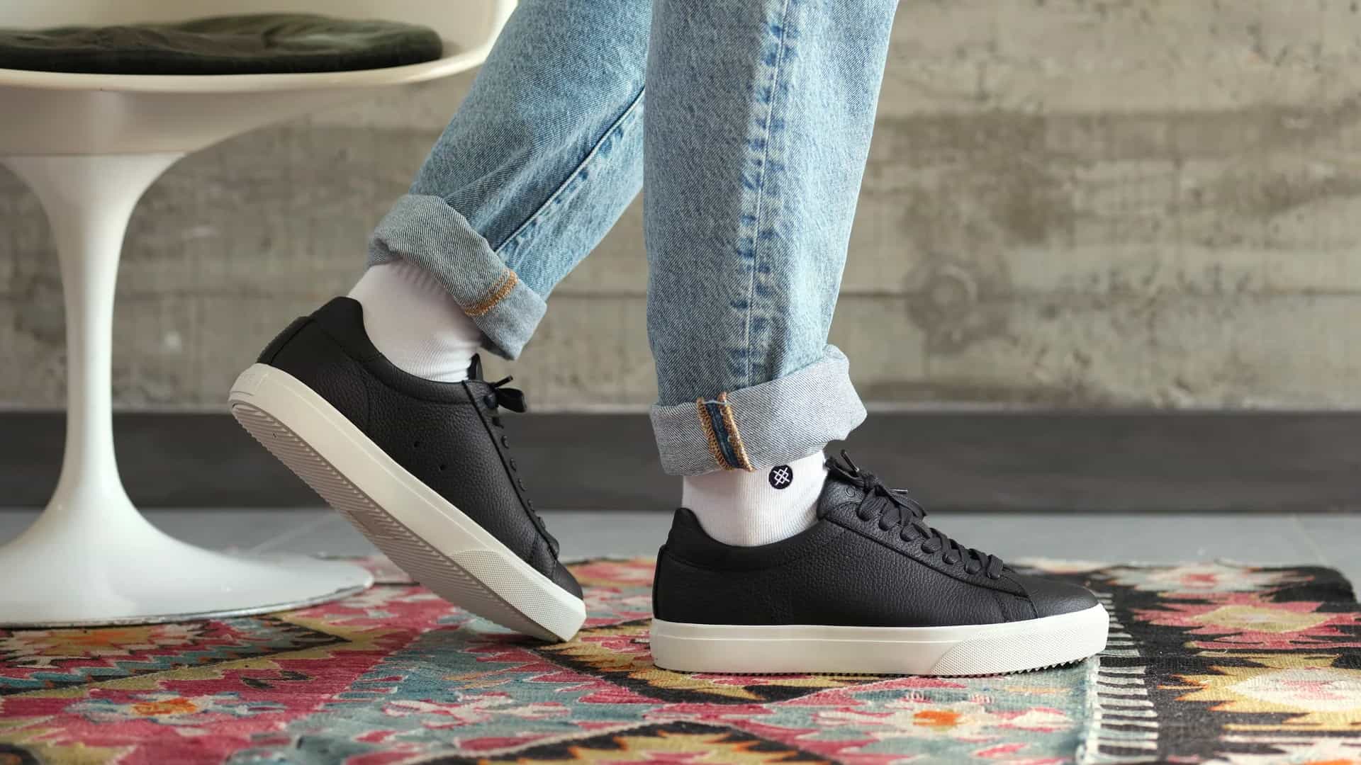 Man wearing CLAE sustainable black leather sneakers on feet with white socks and light wash jeans turned up