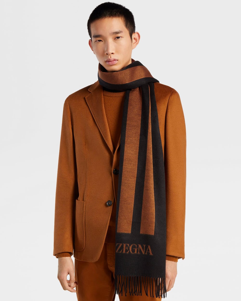 Man wearing a brown-orange blazer, pants and a black and brown Zegna scarf