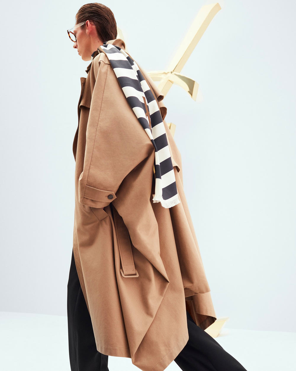 Man wearing oversized camel trench coat and black-white stripe Saint Laurent scarf