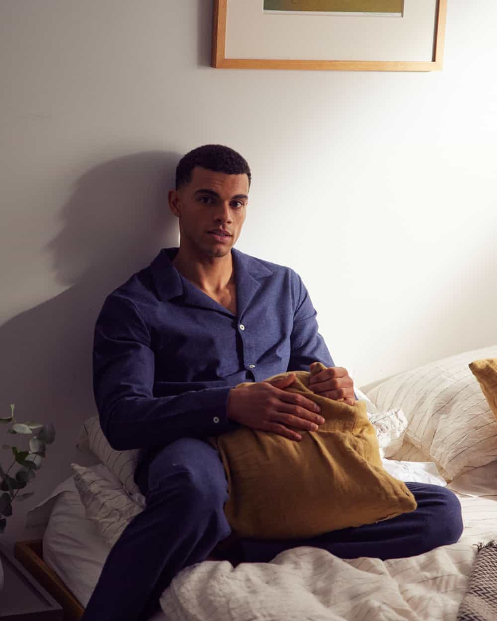 Man sitting in bed wearing matching button up camp collar pajamas in blue by Hamilton and Hare