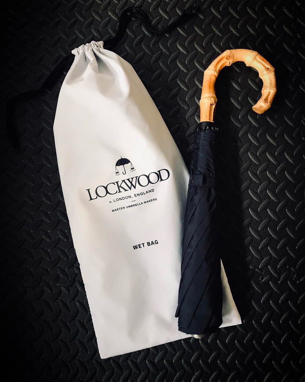 A luxury Lockwood Umbrella with wooden handle and navy canopy next to its branded storage bag