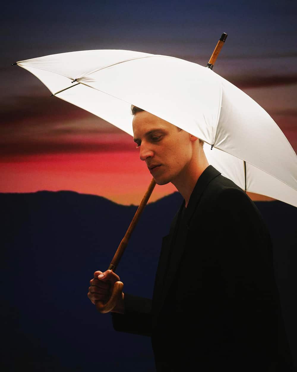 Man in black overcoat holding a Swaine wooden handle umbrella with white fabric canopy