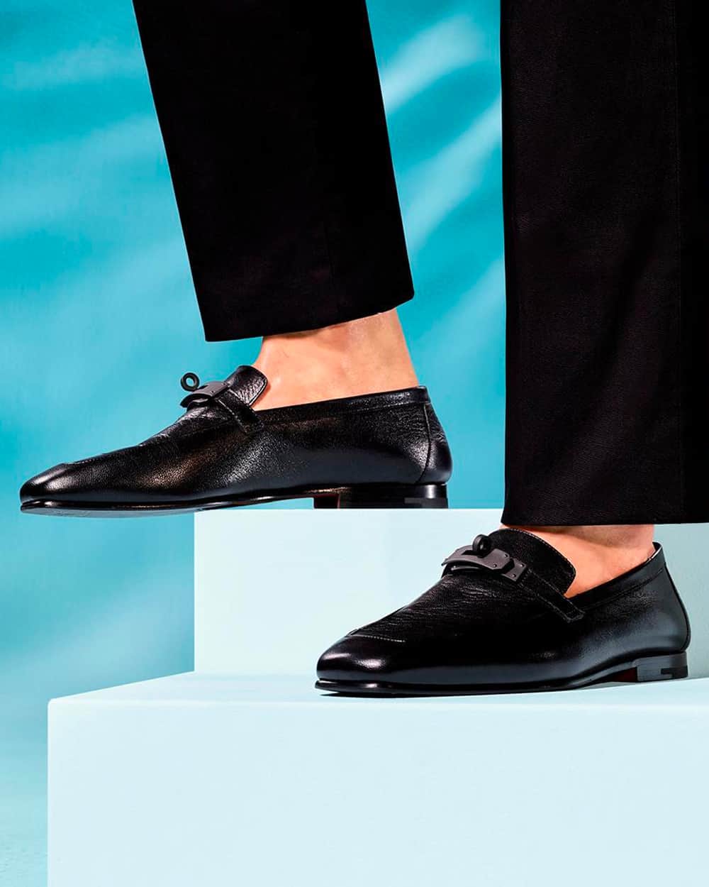 Man wearing black leather Hermes loafers on feet sockless with black pants