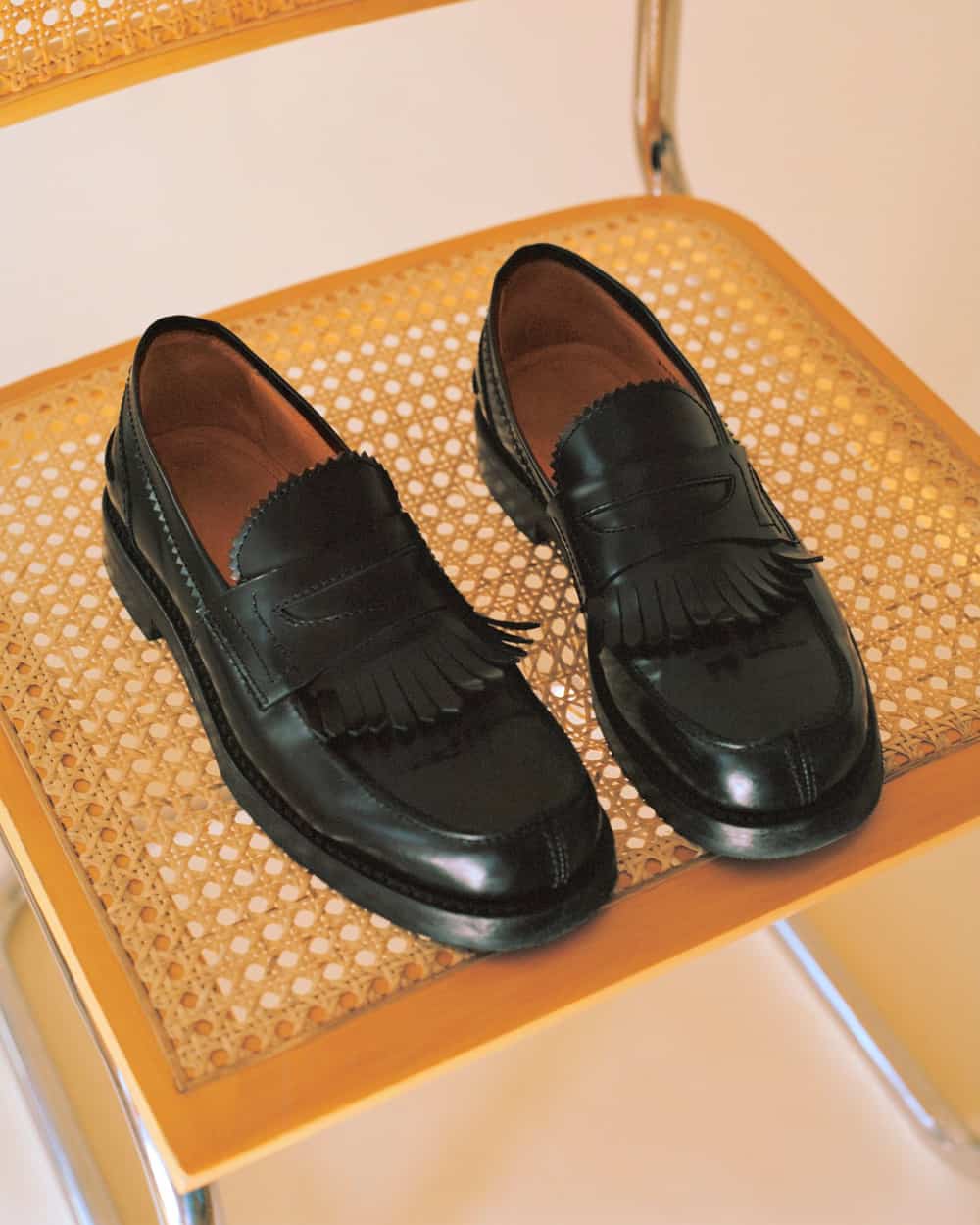 A pair of men's black leather fringed loafers by Our Legacy set on chair