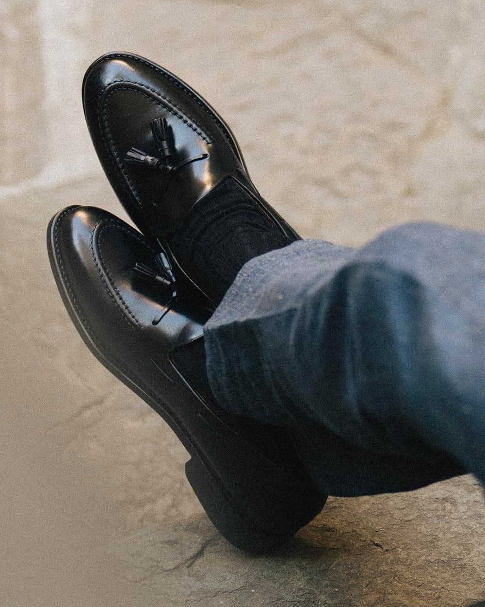 Man wearing a pair of high end black leather tassel loafers by Velasca with black socks and grey wool pants