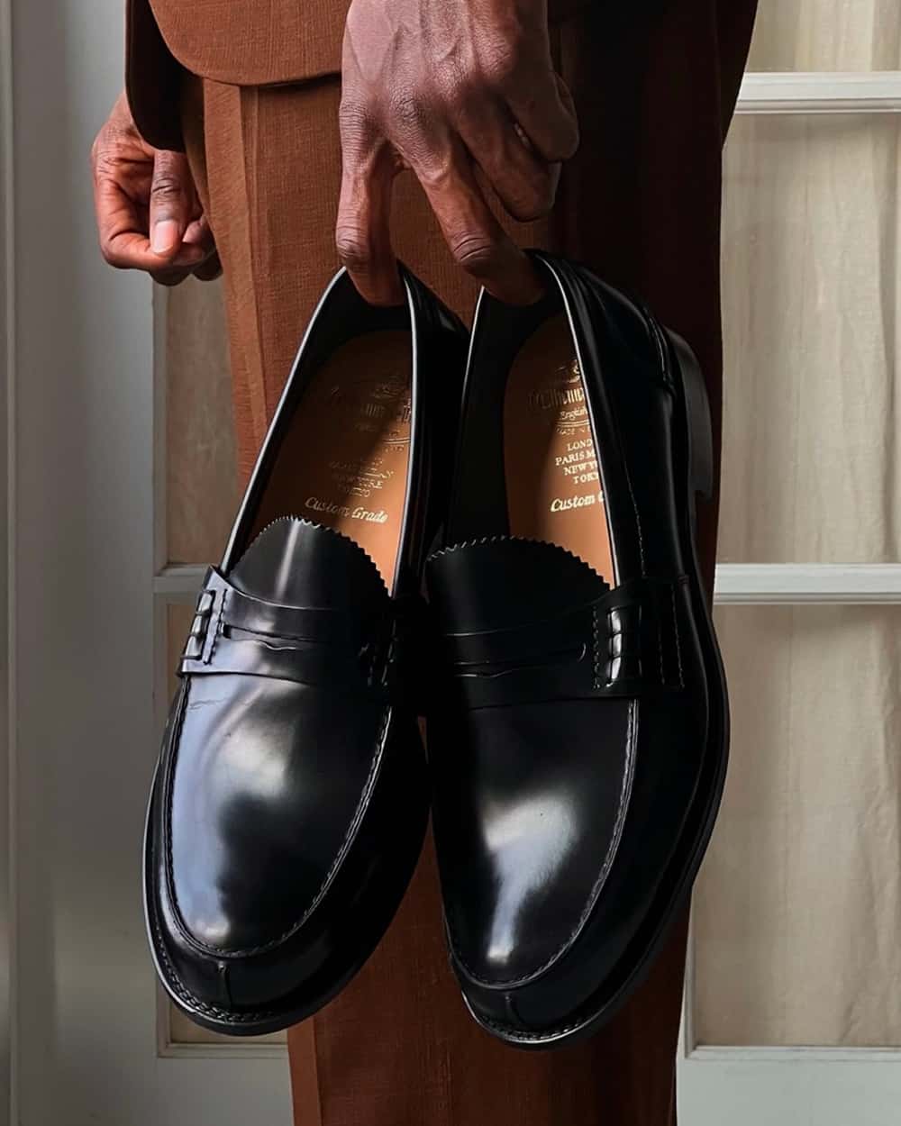 Man in brown suit holding a pair of luxury Church's black leather penny loafers