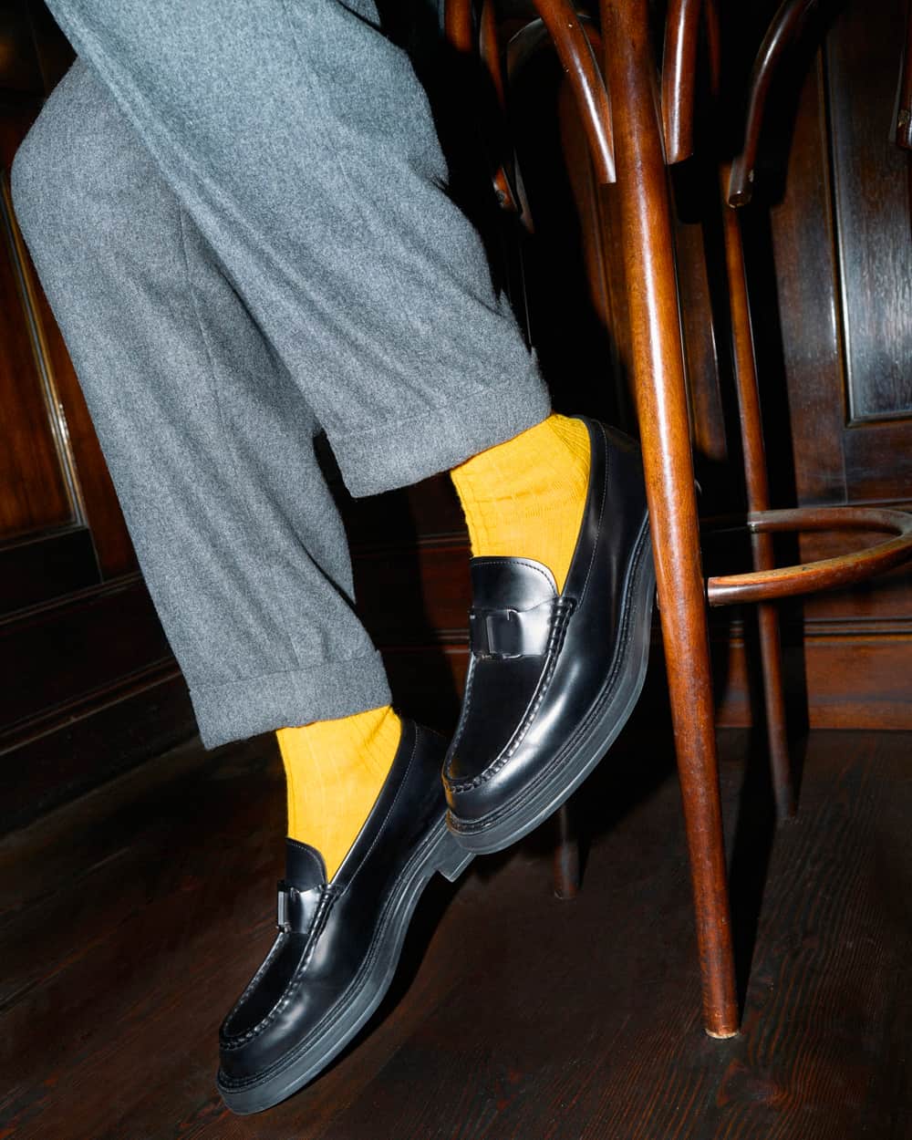 Man wearing Tod's black leather loafers with bright yellow socks and grey wool pants