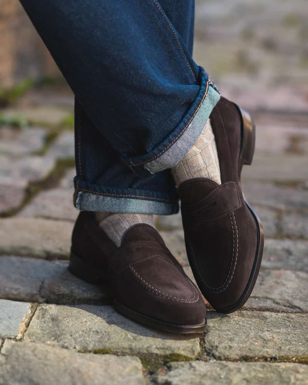 Man wearing brown suede Loake penny loafers with beige socks and blue turned up jeans