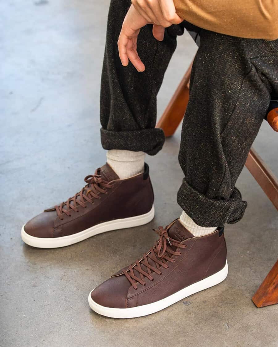 CLAE Bradley Mid Cocoa Leather sneaker worn on feet with white socks and grey flannel pants