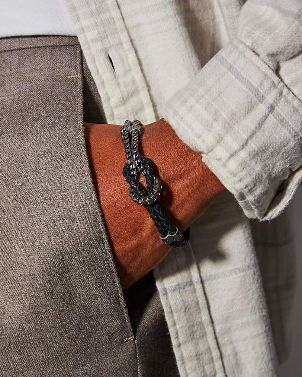 Man wearing grey pants, white T-shirt and off-white check shirt with a Marco dal Maso luxury rope knot bracelet