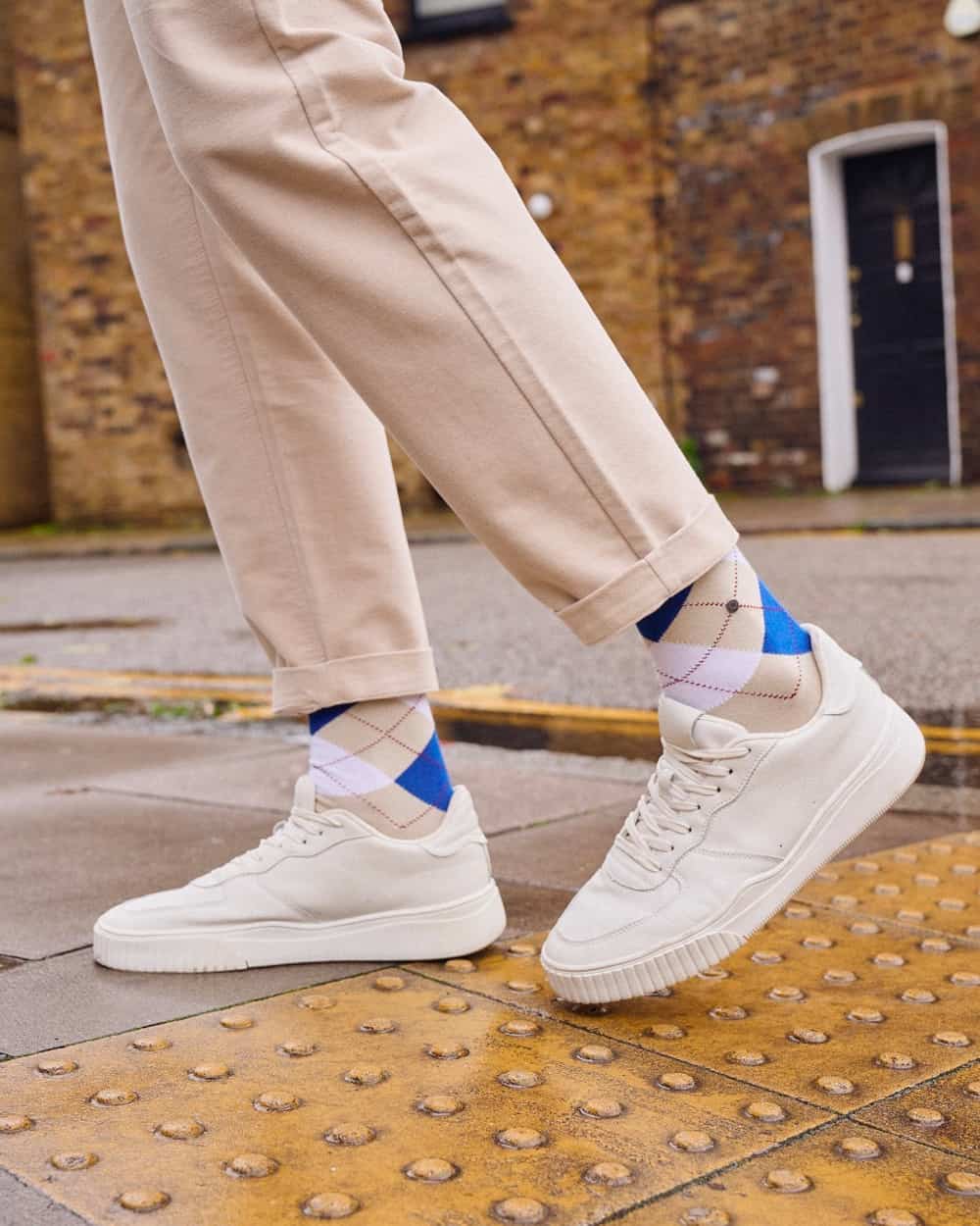 Man wearing luxury Falke argyle print socks on feet with turned up beige pants and white sneakers