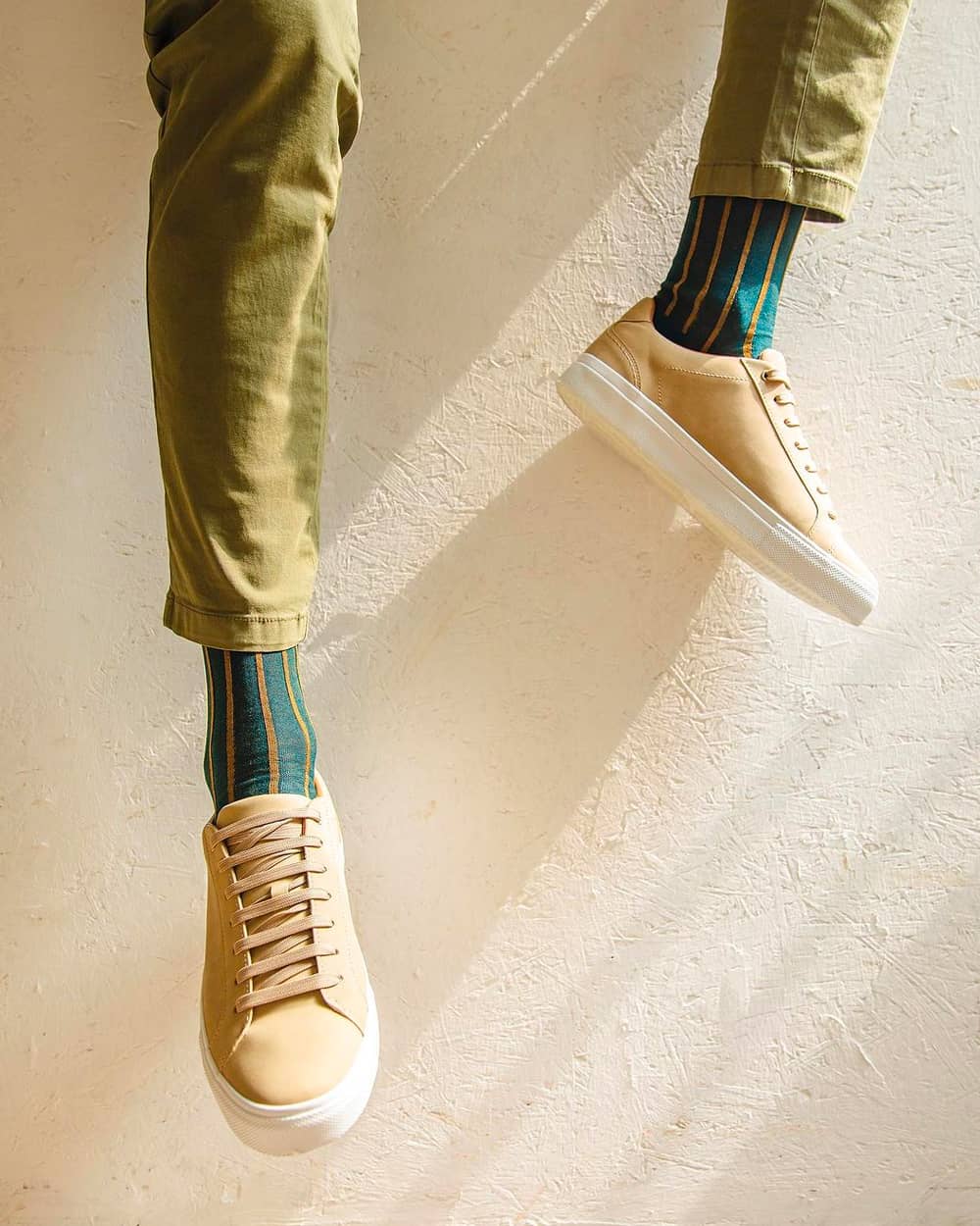 Man wearing luxury teal and yellow stripe Gallo socks on feet with green pants and yellow-beige sneakers