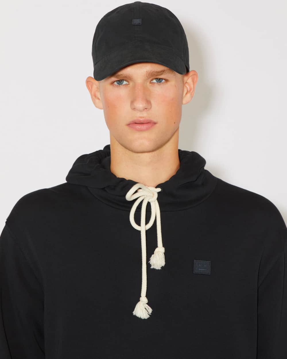 Man wearing black Acne Studios hoodie with black baseball cap