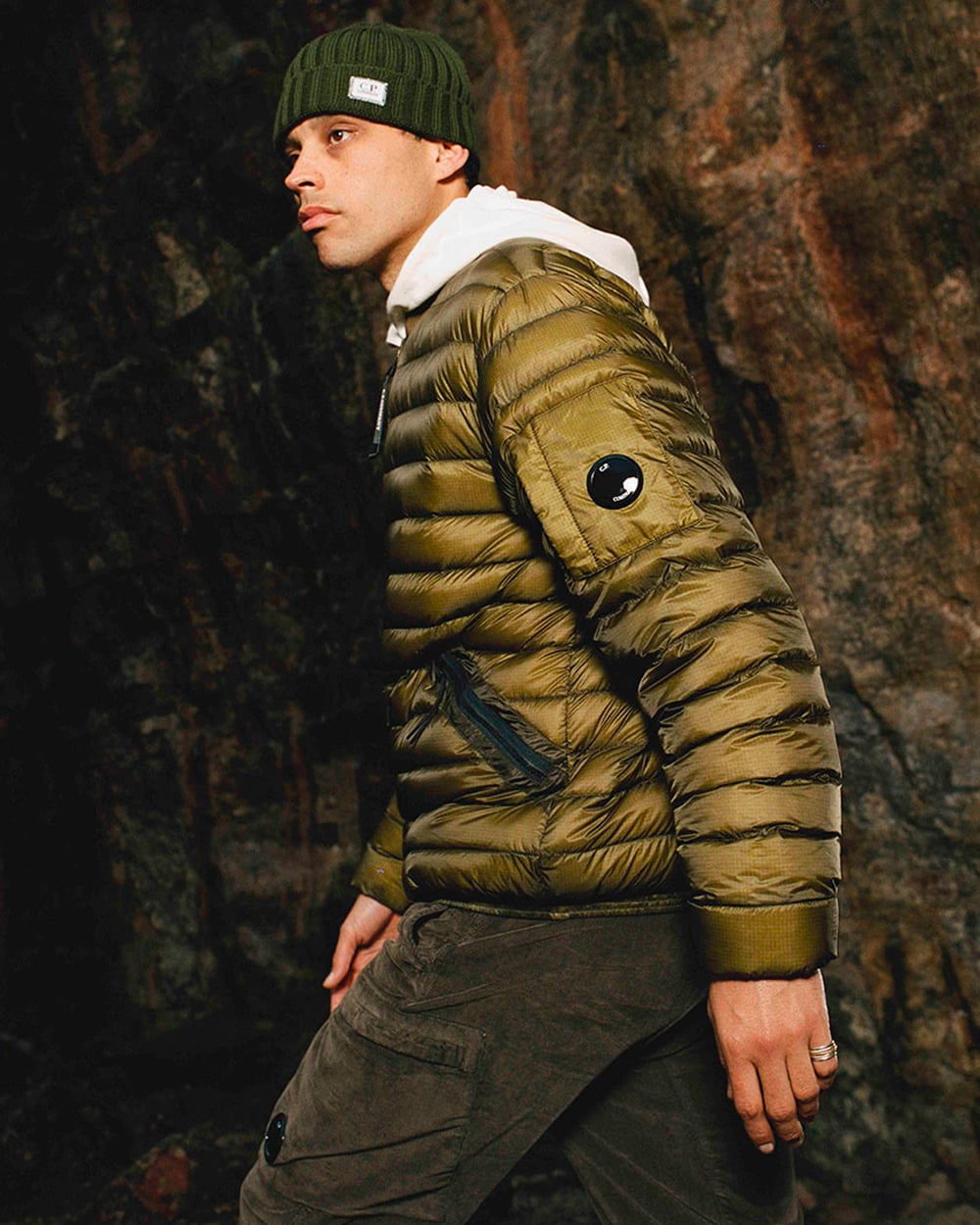 Man wearing C.P. Company olive green cargo pants, white hoodie, green puffer jacket and green beanie