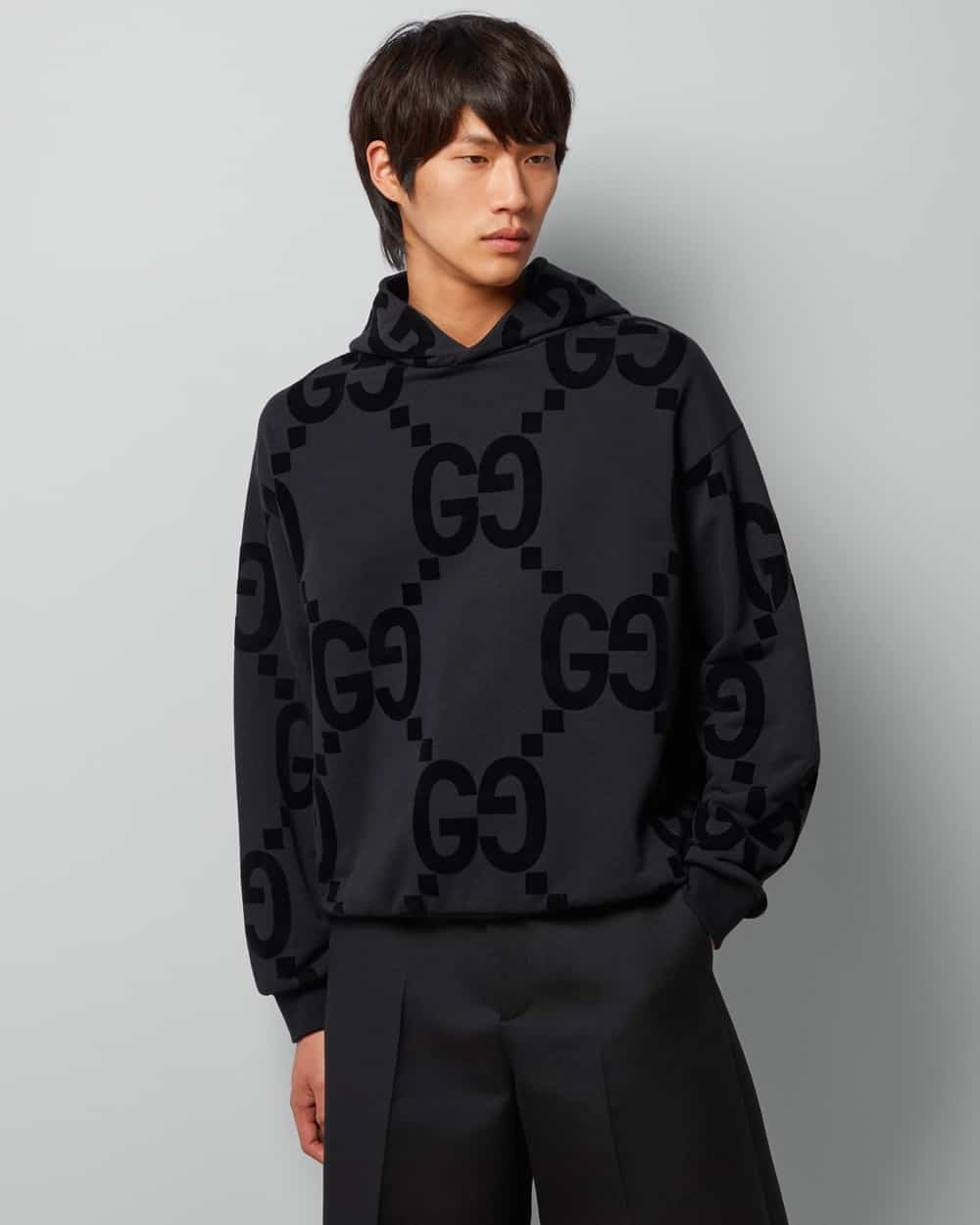 Asian man wearing a black Gucci logo monogram hoodie with loose black pants