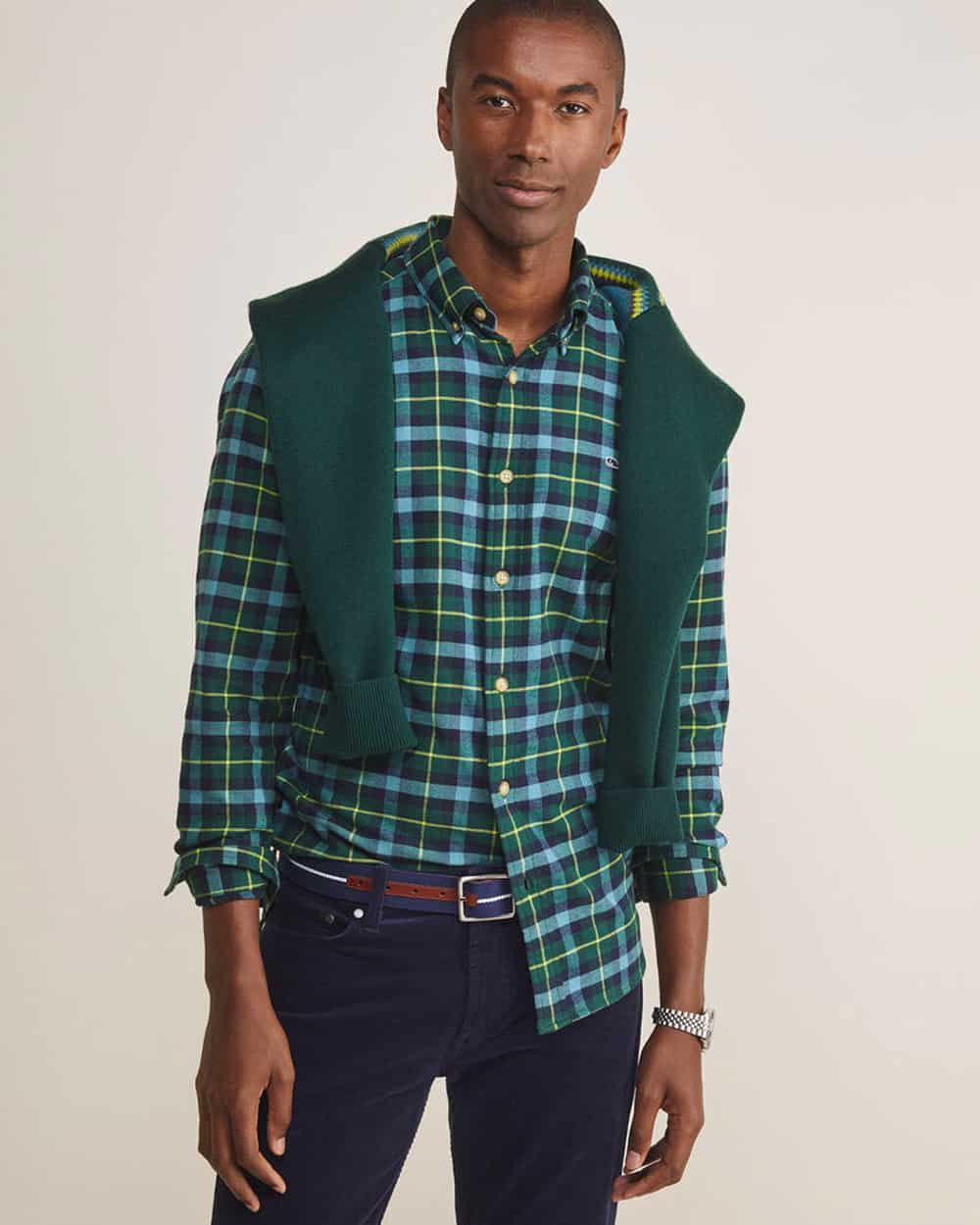 Man wearing Vineyard Vines navy pants, blue/green check shirt and green sweater over shoulders