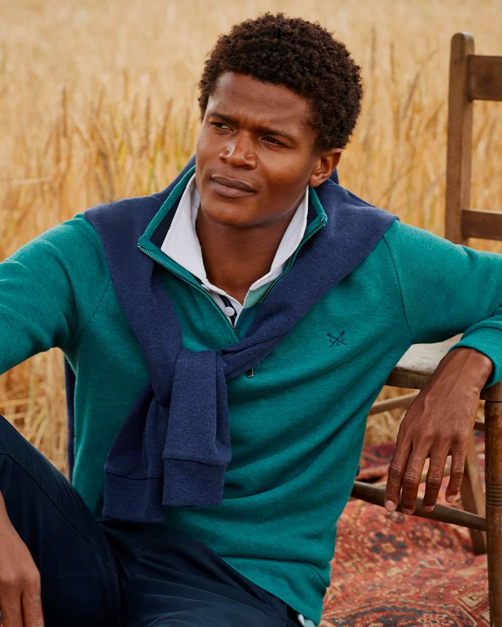 Black man wearing crew Clothing white rugby shirt, teal quarter-zip sweater and navy pants
