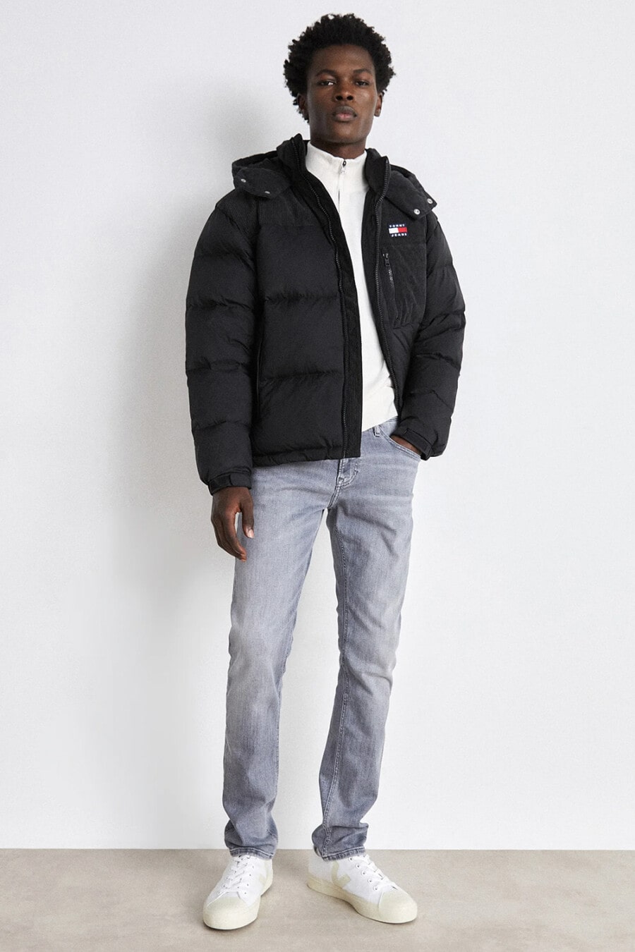 Men's light grey jeans, white zip-up cardigan, black puffer jacket and white sneakers outfit