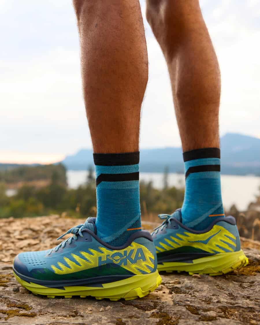 Man wearing light blue and yellow Hoka One One running trail sneakers outdoors with bright blue socks