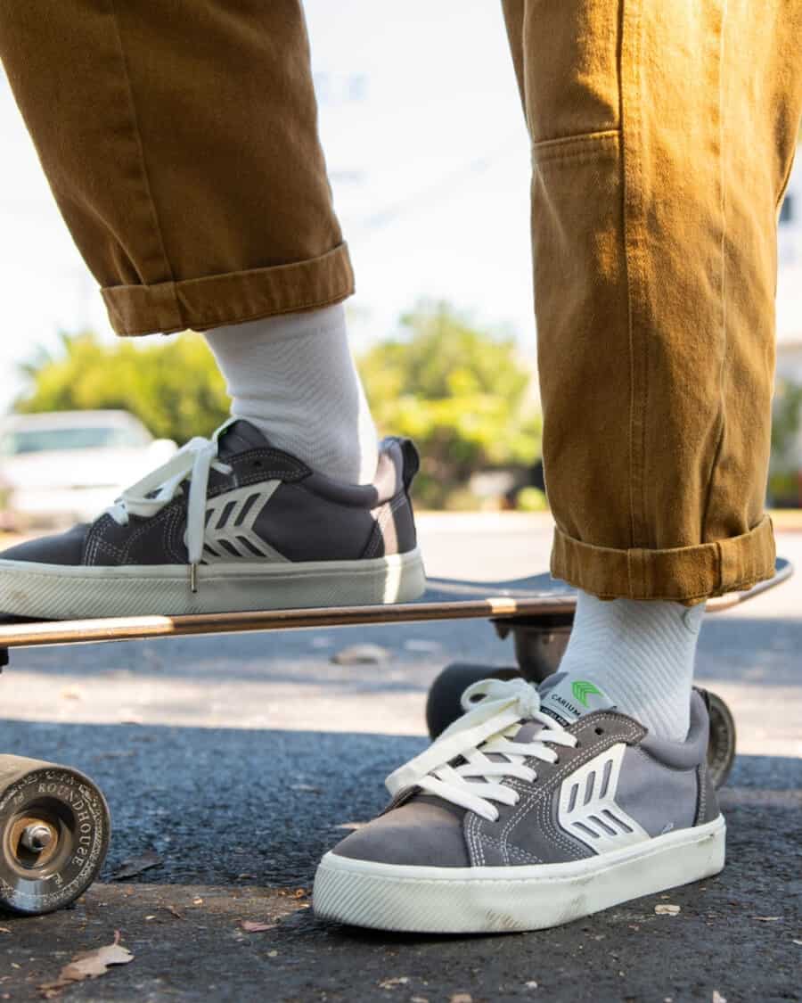 Man wearing grey canvas Cariuma skate shoe sneakers on feet with white socks and khaki worker pants with a skateboard