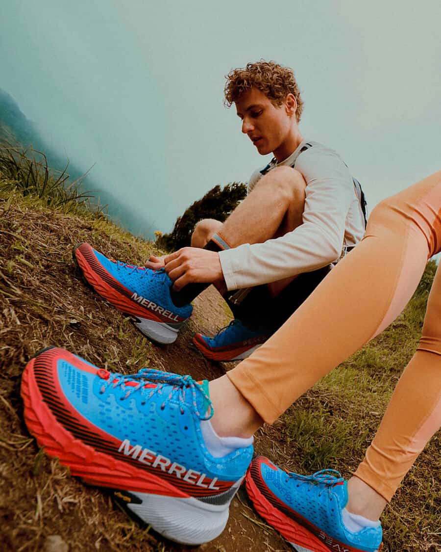 Two people outdoors on a hike wearing blue, red and white chunky Merrell hiking sneakers